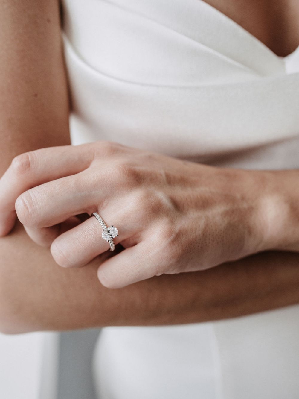 Hand mit Verlobungsring am weißen Kleid