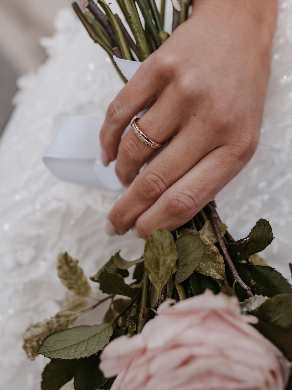 Hand der Braut mit Trauring, Blumenstrauß im Arm