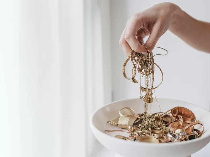 Hand hält goldene Ketten über eine Schale mit Altgold, Ringen und Schmuck — Goldankauf beim Juwelier Otto Parr in Gießen