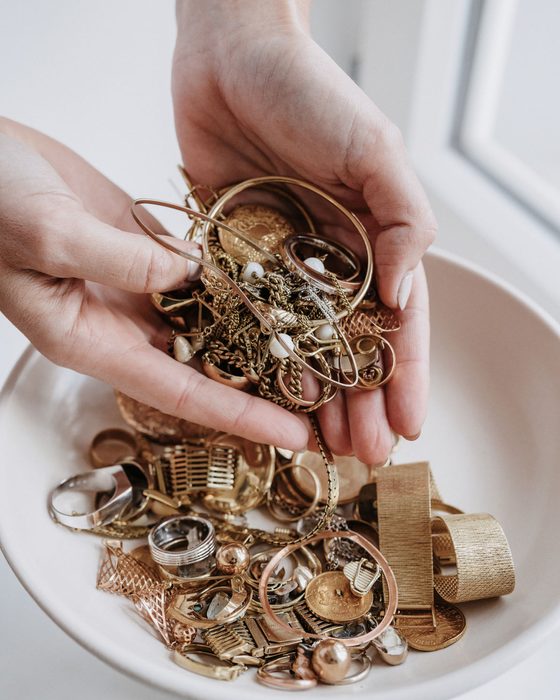 Zwei Hände halten eine Handvoll Altgold über einer weißen Schale — geprüft wird auf dem Tresen