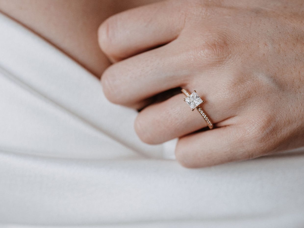 Hand mit einem Verlobungsring über dem weißen Brautkleid