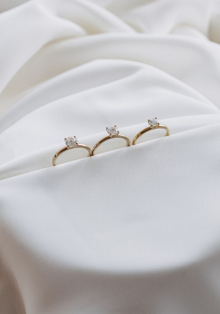 Drei schmale Solitärringe aus Gelbgold nebeneinander auf weißem Satin