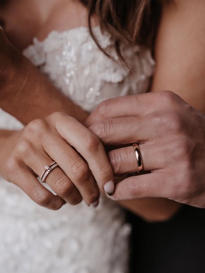 Hände des Brautpaars nebeneinander, ihr schmaler Memoire-Ring und sein breiter Trauring in Roségold
